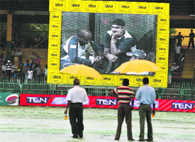 Sri Lankan ground staff holding umbrellas look at a screen at Premadasa Stadium in Colombo on Tuesday. Heavy persistent downpour resulted in the fourth one-day international match between Sri Lanka and India being washed out on Tuesday. The match will be played on Wednesday.