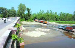Vehicles pass through the dry riverbed beside the damaged bridge. Photo: Vinod Pundir