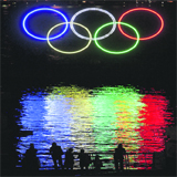 People stop to look at a tall set of Olympic rings after being illuminated in the harbor outside the Vancouver Convention Centre in Vancouver, B.C.