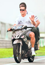 Mercedes Formula One driver Michael Schumacher rides a motorbike towards the pit lane at the Sepang F1 circuit outside Kuala Lumpur on Thursday