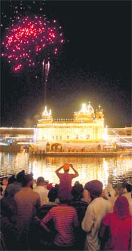 Devotees watch fire crackers over illuminated Golden Temple on the occasion of the birth anniversary of Guru Ram Dass, the fourth Sikh guru who founded Amritsar city, in Amritsar on Sunday.