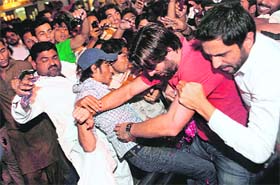Shahid Afridi (2nd R) pushes his way past fans at the airport following his return to Karachi on Friday