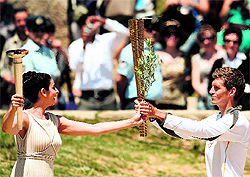 Actress Ino Menegaki (L), acting as high priestess, passes the Olympic flame to the first torch bearer Spyros Gianniotis during the lighting ceremony in ancient Olympia, where the Olympic Games were born in 776 B.C., on Wednesday