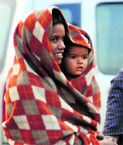 A woman covers her child in a blanket to protect her from the cold waves blowing in Karnal.