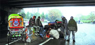 Rickshaw-pullers sit around a bonfire to keep themselves warm under a flyover after a shower in Karnal recently.