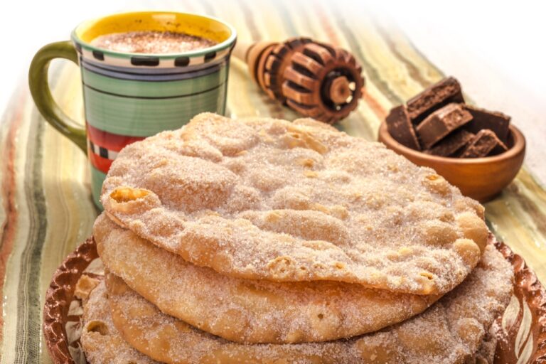 a pile of three Mexican buñuelos with a clay cup