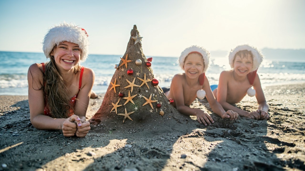 A woman and two children lying on a Cabo beach in Christmas caps and tree