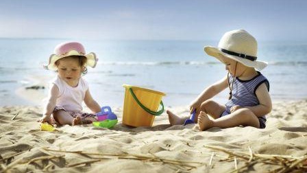 babygirl and babyboy sitting on the beach in straw hats