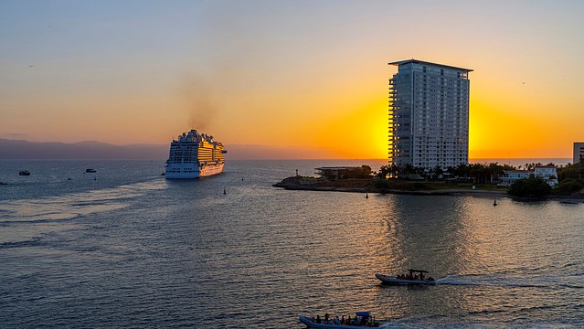 Sunset evening view from a cruise ship balcony of the cruise port skyline and sea as a cruise ship sails away in the distance at Puerto Vallarta, Mexico