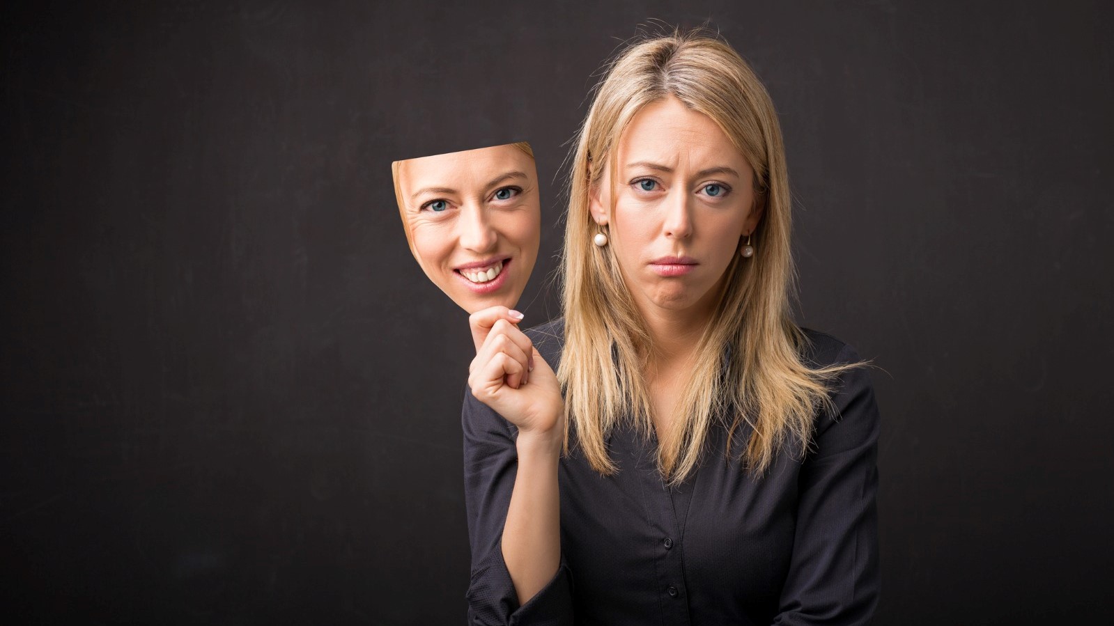 Sad woman holding a happy mask of herself