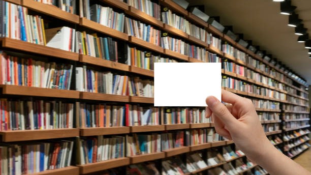 A female hand holding a white card in front of a bookcase