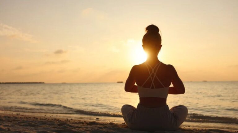 Woman sitting in yoga position in front of the setting sun.