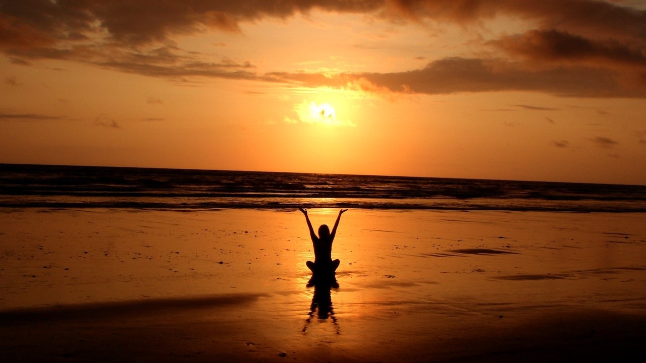 A person meditating on the beach at sunset