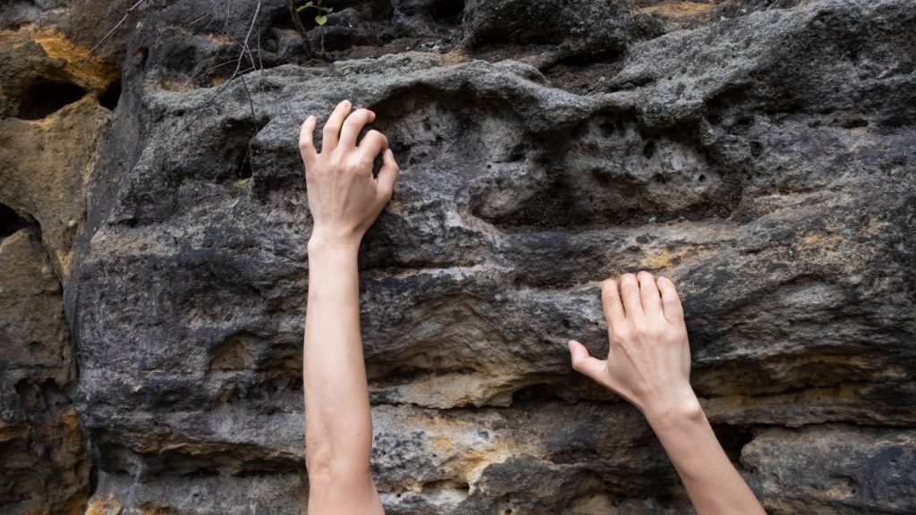 Two hands holding onto rock wall