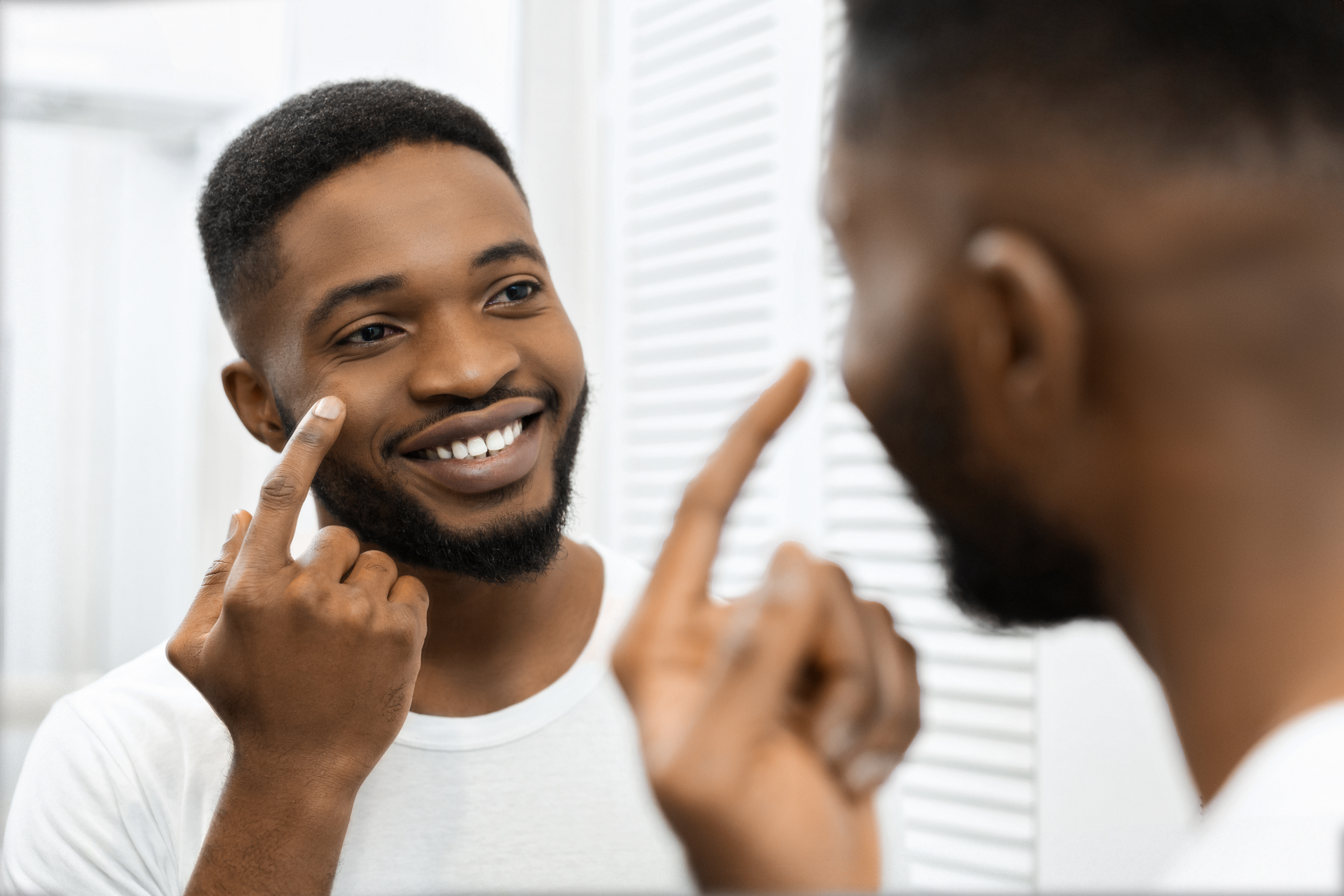 Man smiling applying face cream in mirror in bathroom.