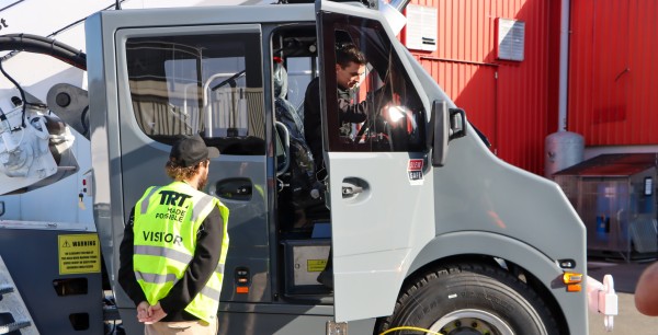 A man in a high vis vest, standing out side of a TIDD crane, talking with the driver