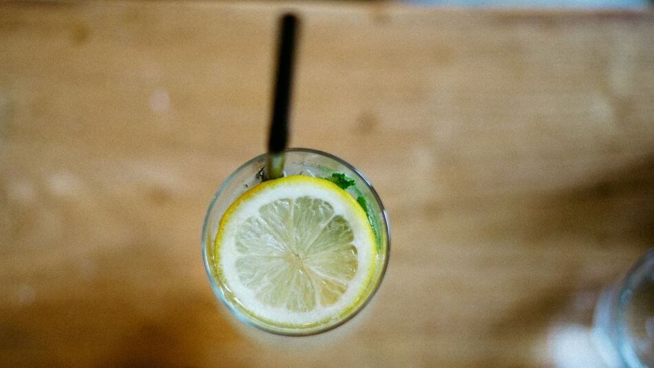 Water glass with lemon and straw, view from above