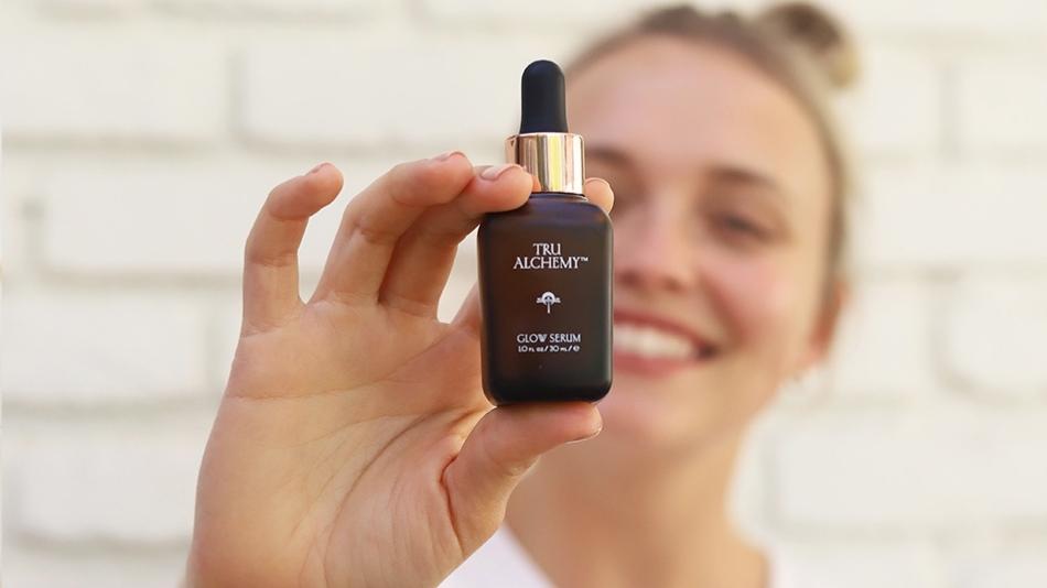 A woman holding Tru Alchemy® Glow Serum bottle