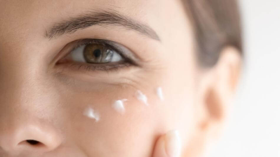 Woman using skin moisturizer ender her eyes