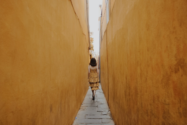 Woman in frilly yellow dress walking down narrow alley of yellow walls