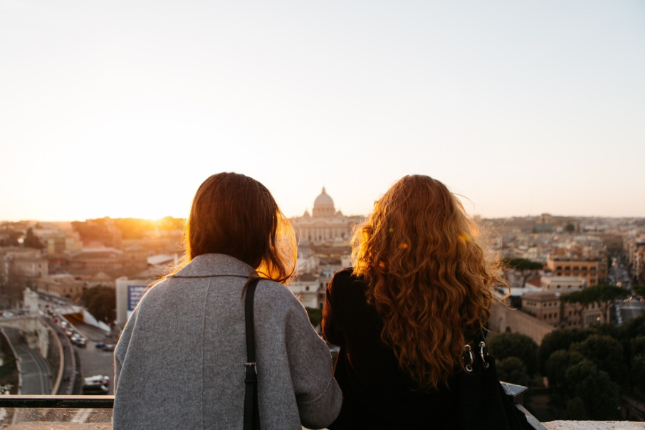 Two women looking over a rooftop view of a city with the sun setting