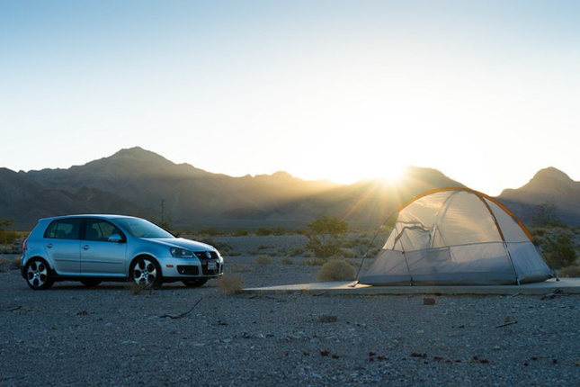 Car and tent bathed in light in front of hills in Death Valley