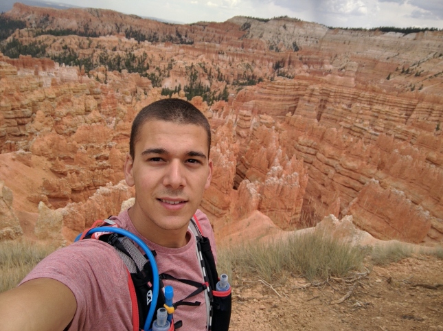 Man in pink shirt with hiking equipment in front of Brice Canyon