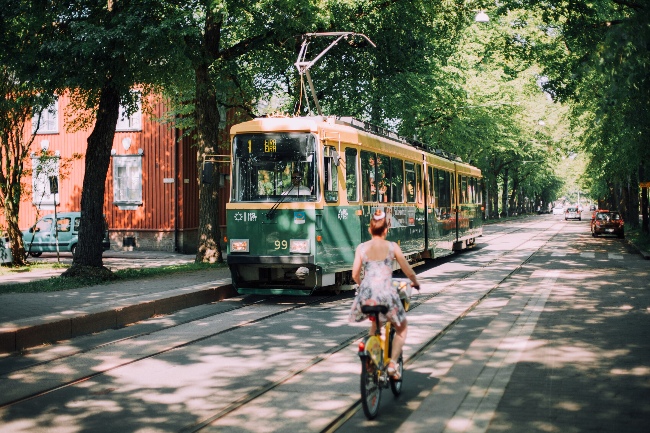 Tram passes woman on bike along tree-lined Helsinki street