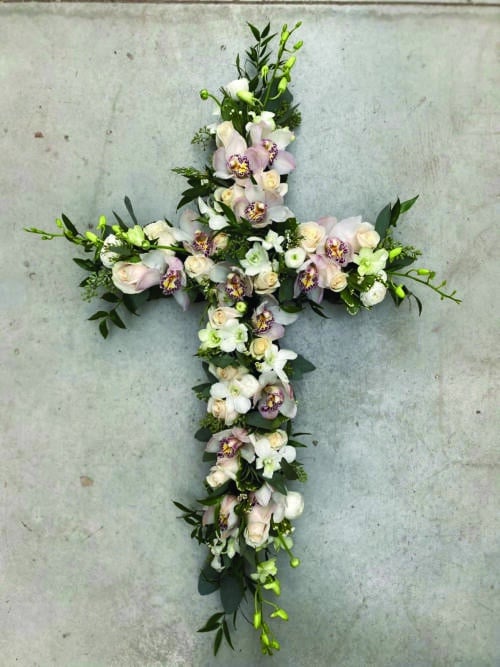 The Watering Can | A soft pink and white flowered cross featuring cymbidium orchids, debdrobium rochids, roses, and ranunuculus.