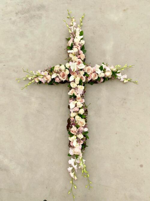 The Watering Can | A large soft pink and white flowered cross featuring roses, cymbidium orchids, dendrobium orchids, and calla lilies.