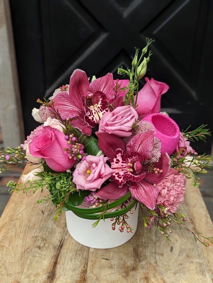 The Watering Can | A hot pink European style arrangement featuring dark pink cymbidium blooms in a white ceramic container with a pink edge.