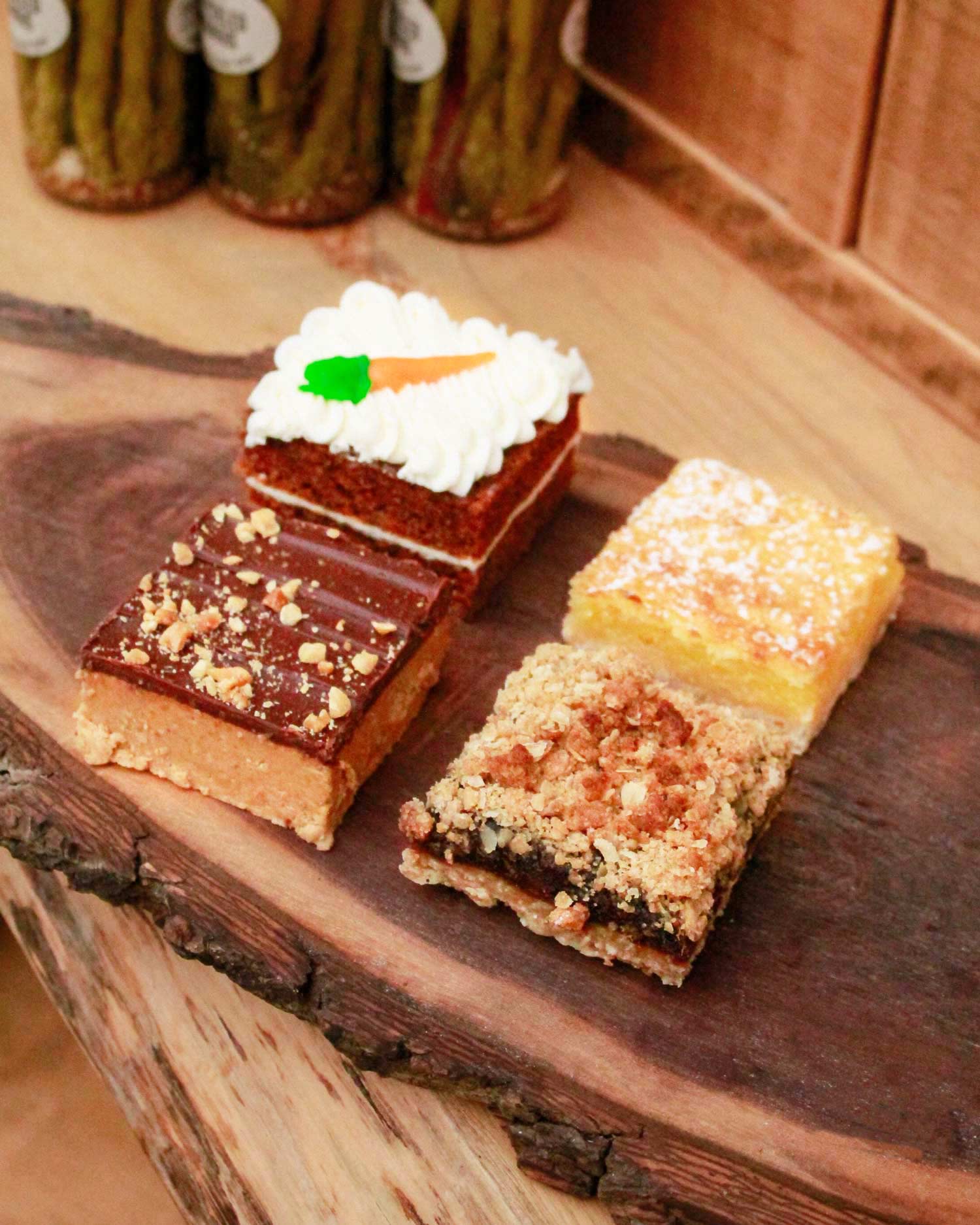 A selection of four assorted baked squares from The Watering Can Pastry Market, showcasing a variety of textures and toppings on a wooden cutting board.