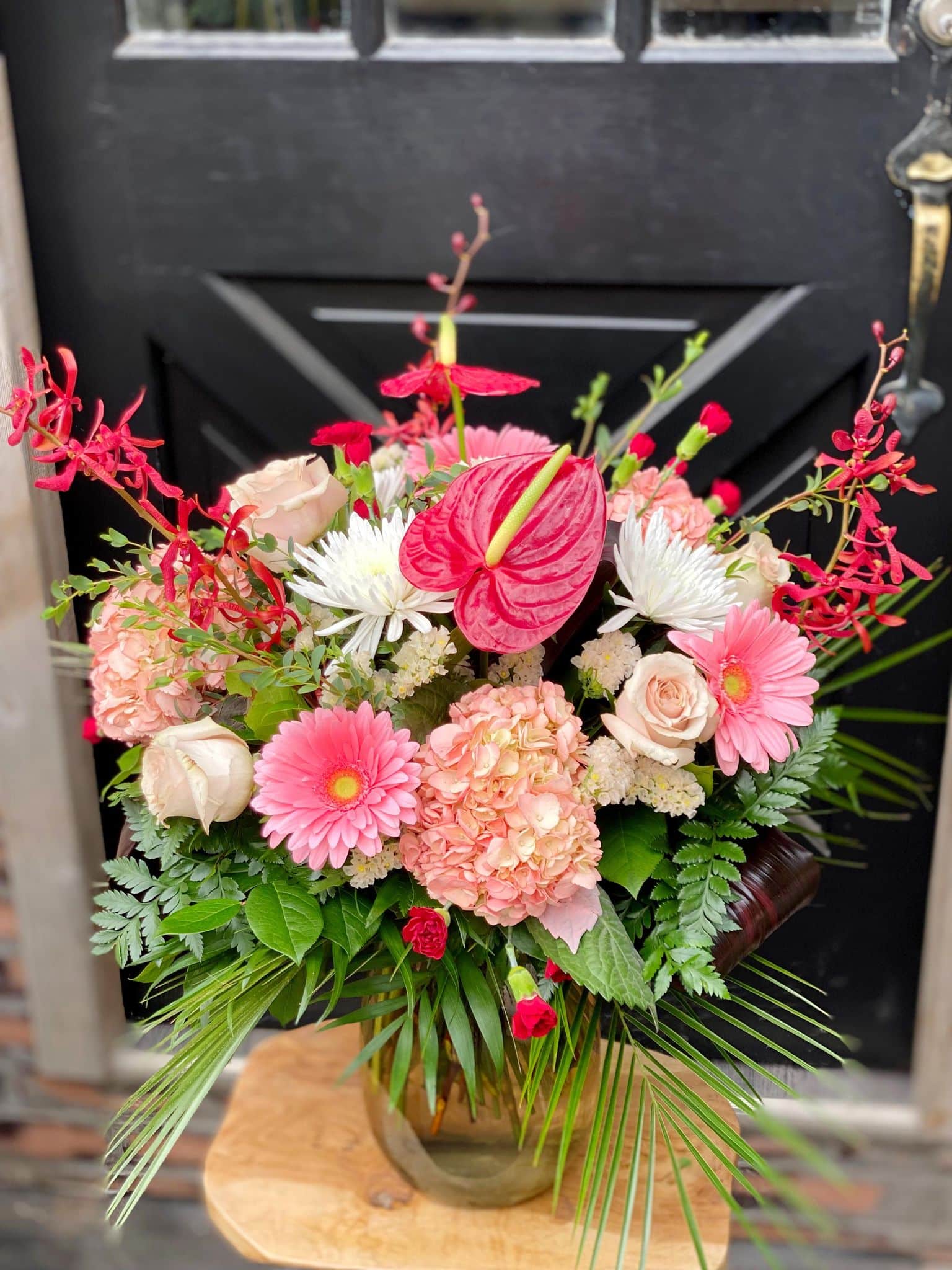 A large monochramtic bouquet in vase ranging from white, through blush to deep reds on a small side table.