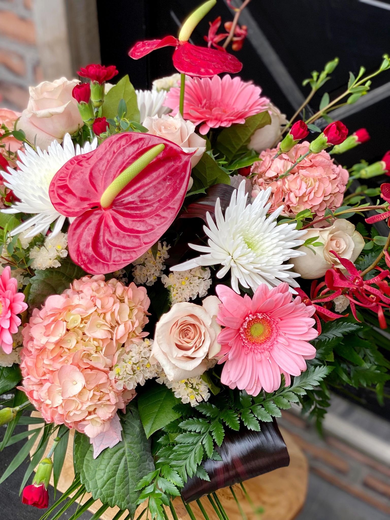 A close up photo of the flowers in a large monochramtic bouquet in vase with a variety of flowers from white, through blush to deep reds.