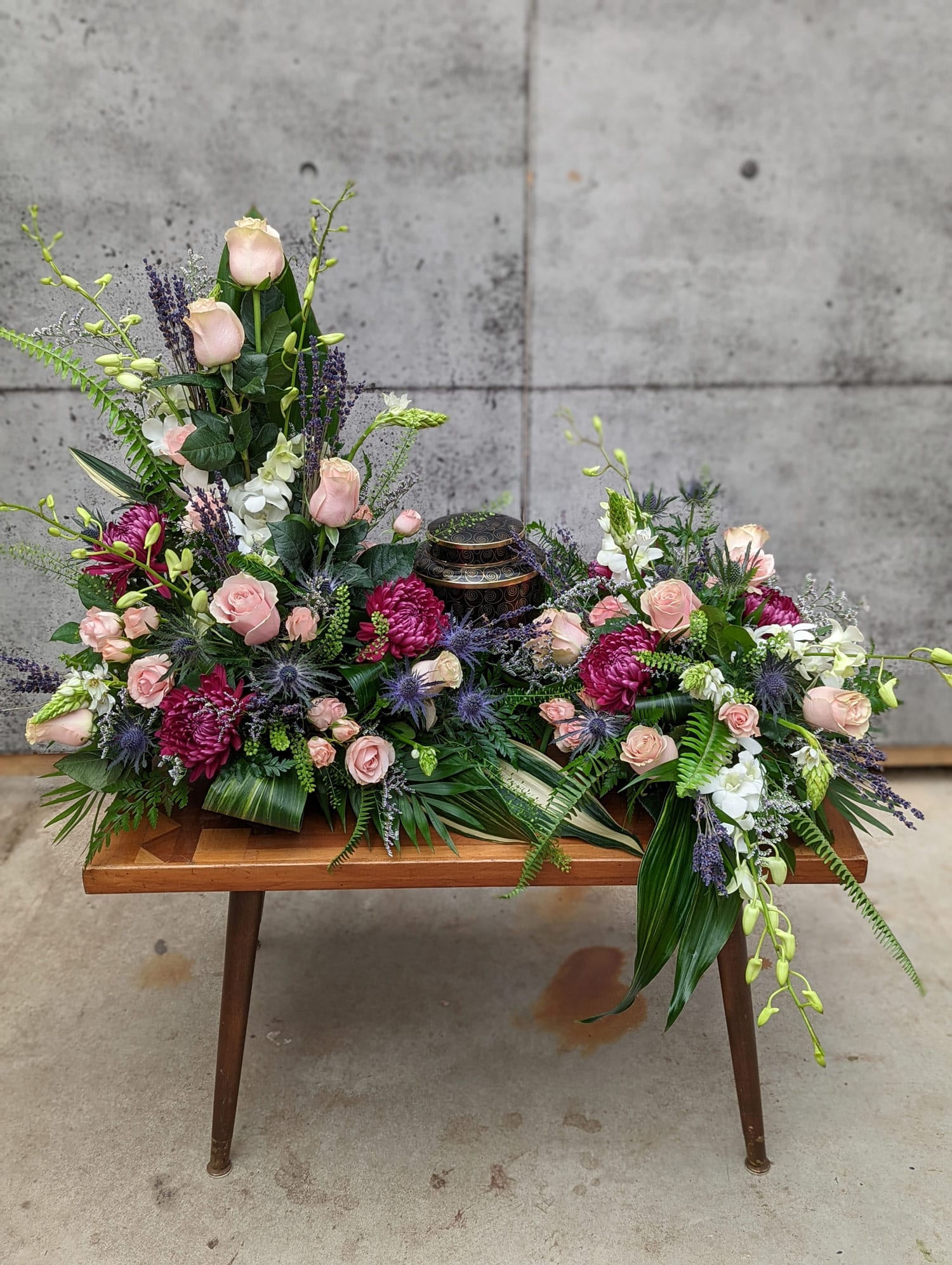 A spectacular blush, plum and blue creamtion design. Soraing above the urn on the right, the arrangement flows around the urn, forwads and down again on the left.