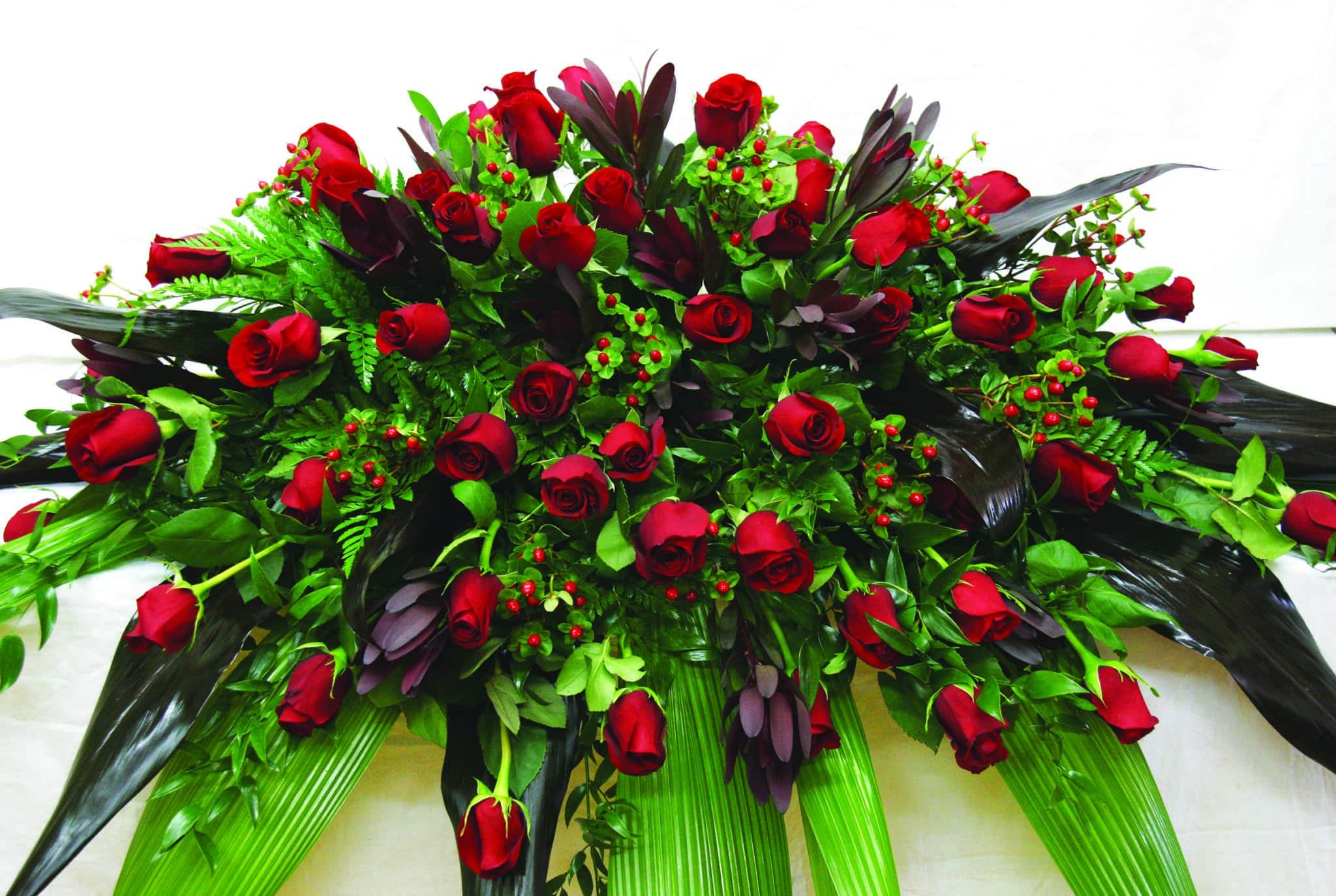 The Watering Can | An all red casket spray with roses, leucadendron, and hypericum flowers in a lush bed of greens.