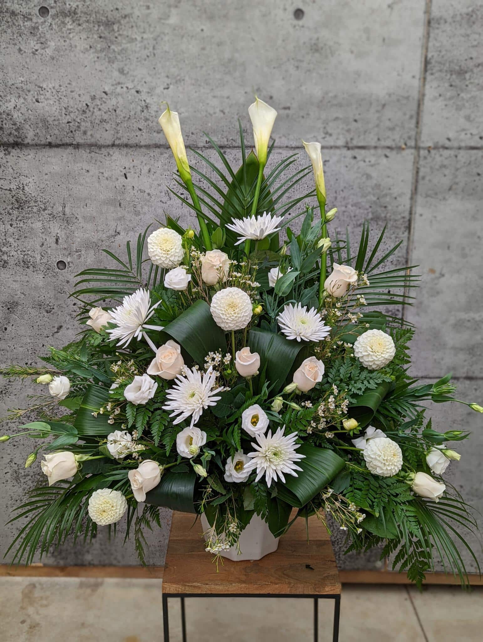 An all white side spray made with calla lilies, dahlias, roses, waxflower, lisianthus, and mums backed by greens.