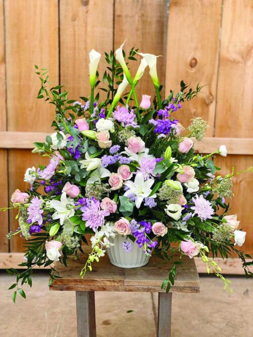 A stunning large and full side spray made with white calla lilies, soft pink roses, white lilies, lavender mums, blue statice, queen anne’s lace, lavender stock, white ranunculus, and white dendrobium orchids supported by greenery.