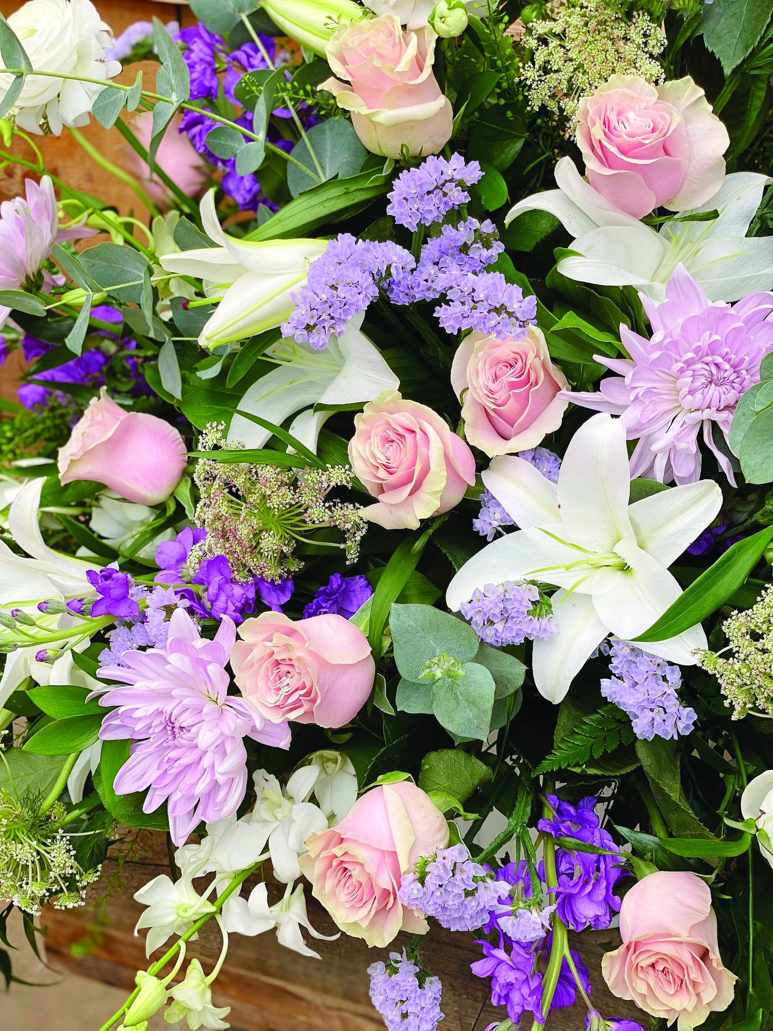 Close up of soft pink roses, white lilies, lavender mums, and blue statice in a side spray.