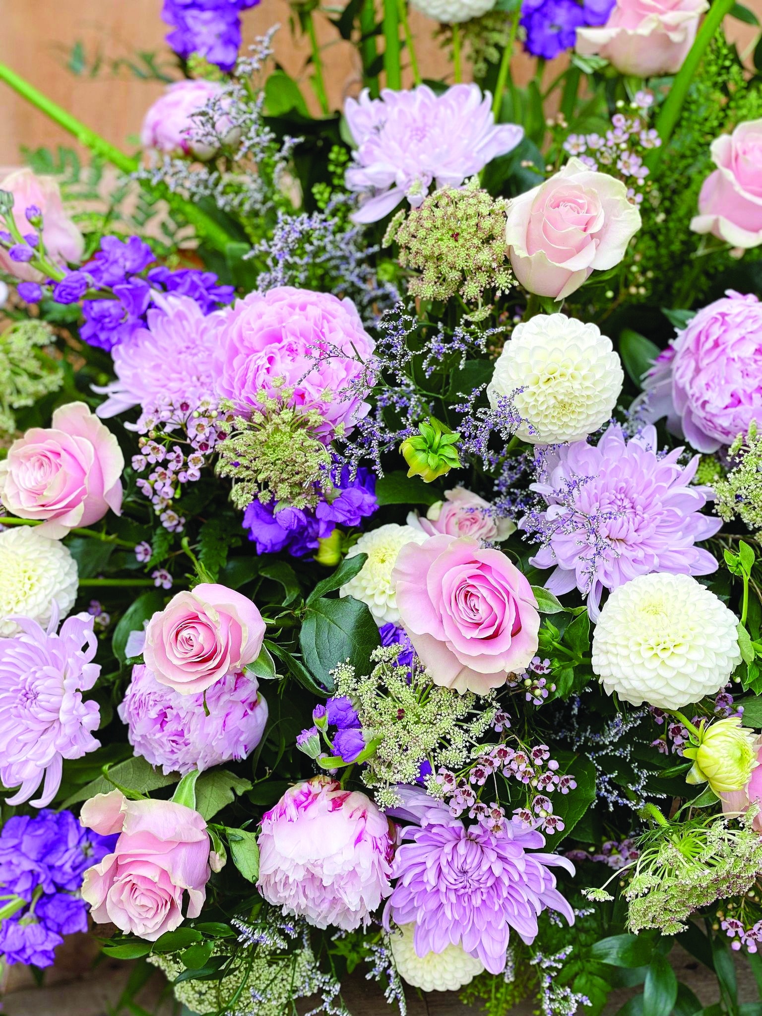 Close up of some soft pink peonies, lavender mums, white dahlias, and soft pink roses in a side spray.