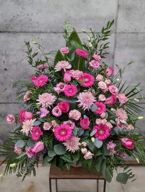 A large pink side spray made with gerberas, lisianthus, mums, roses, carnations, freesias, eucalyptus, and greens.