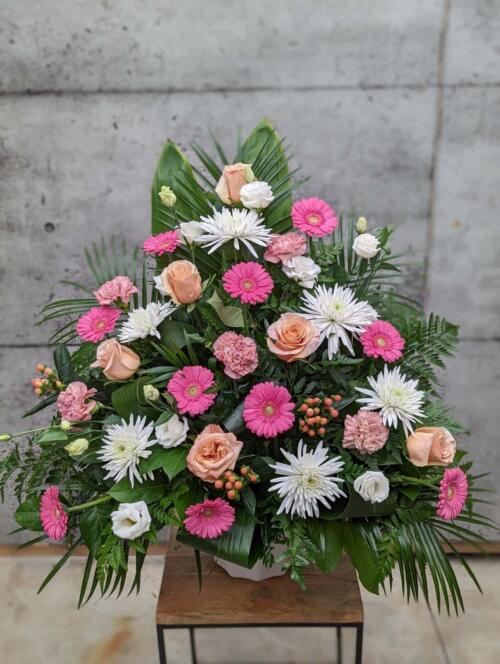 A large peach, pink, and white side spray made with white mums, shimmer roses, pink gerberas, peach hypericum, dusty pink carnations, and white lisianthus backed by greens.