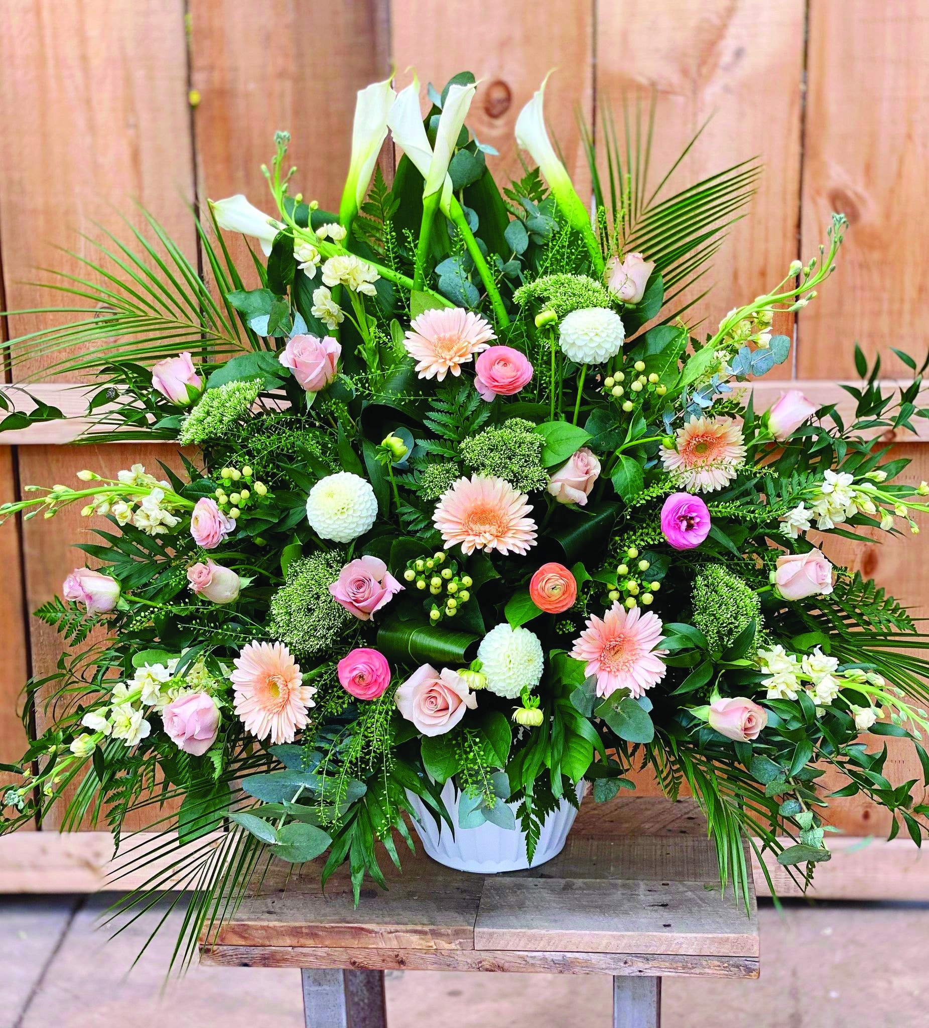 A blush side spray made with white calla lilies, blush roses, white dahlias, cream stock, peach gerberas, white hypericum, peach ranunculus, and white trachelium backed by greens.
