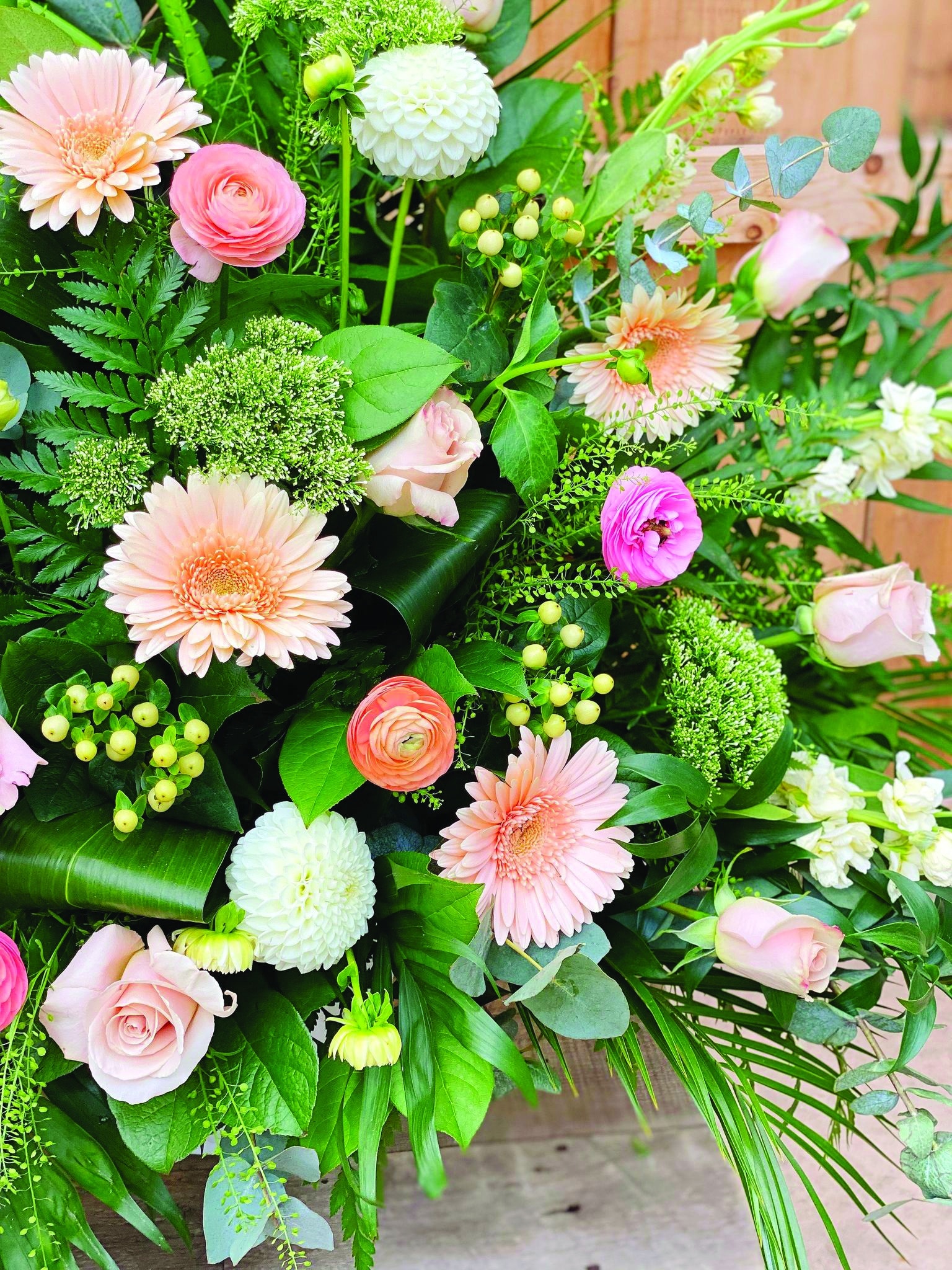 Close up of peach gerberas, runuclus soft pink roses, white hypericum, and white dahlias in a side spray.