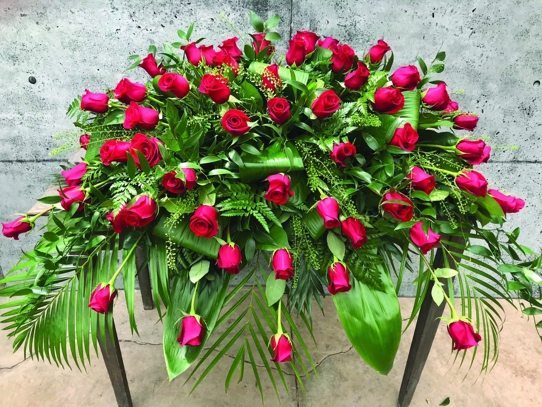 A casket spray made with red roses and a variety of lush greens.