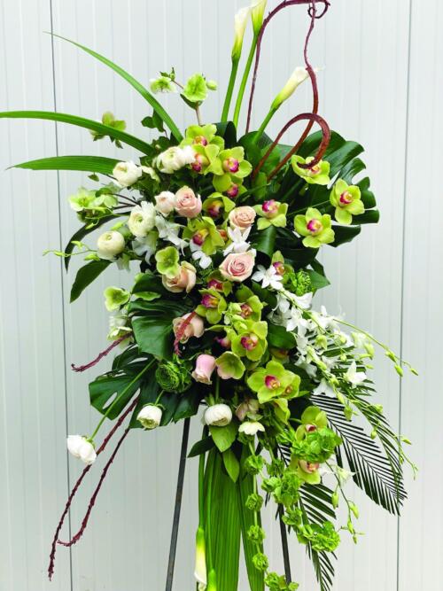 A stunning modern easel spray made with white calla lilies, bells of Ireland, white & green rununculus, white helleborus, green cymbidium orchids, white dendrobium ochids, light pink roses, fantail willow, and tropical greens.