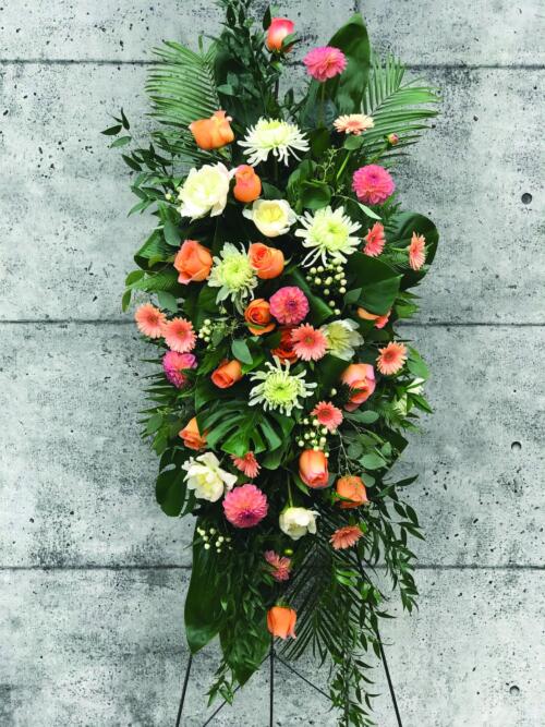 A coral and white easel spray made with coral roses, white mums, peach/coral dahlias, white peonies, peach gerberas, and white hypericum.