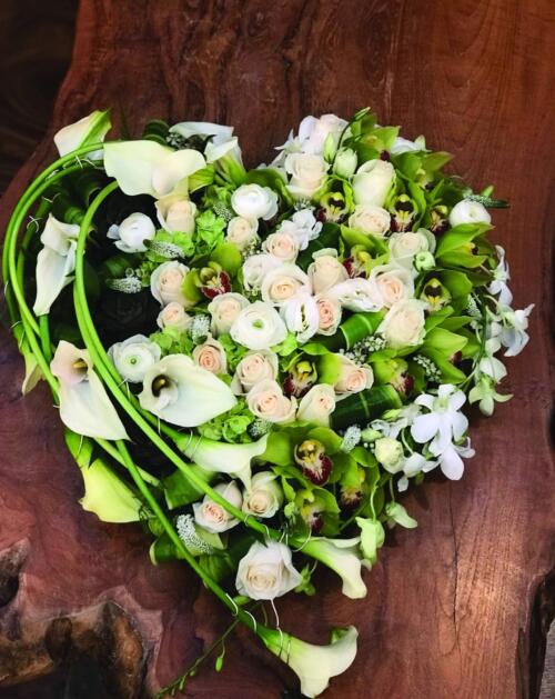 A modern heart design using a variety of white flowers with long calla lilies along one side.