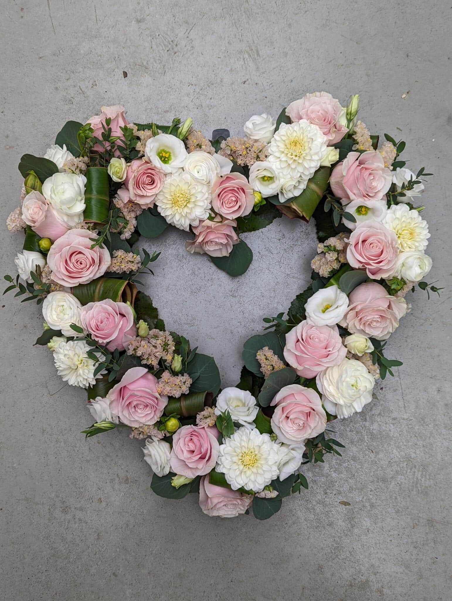 An open pink and white heart filled with roses, dahlias, lisianthus, rununculus, and statice.