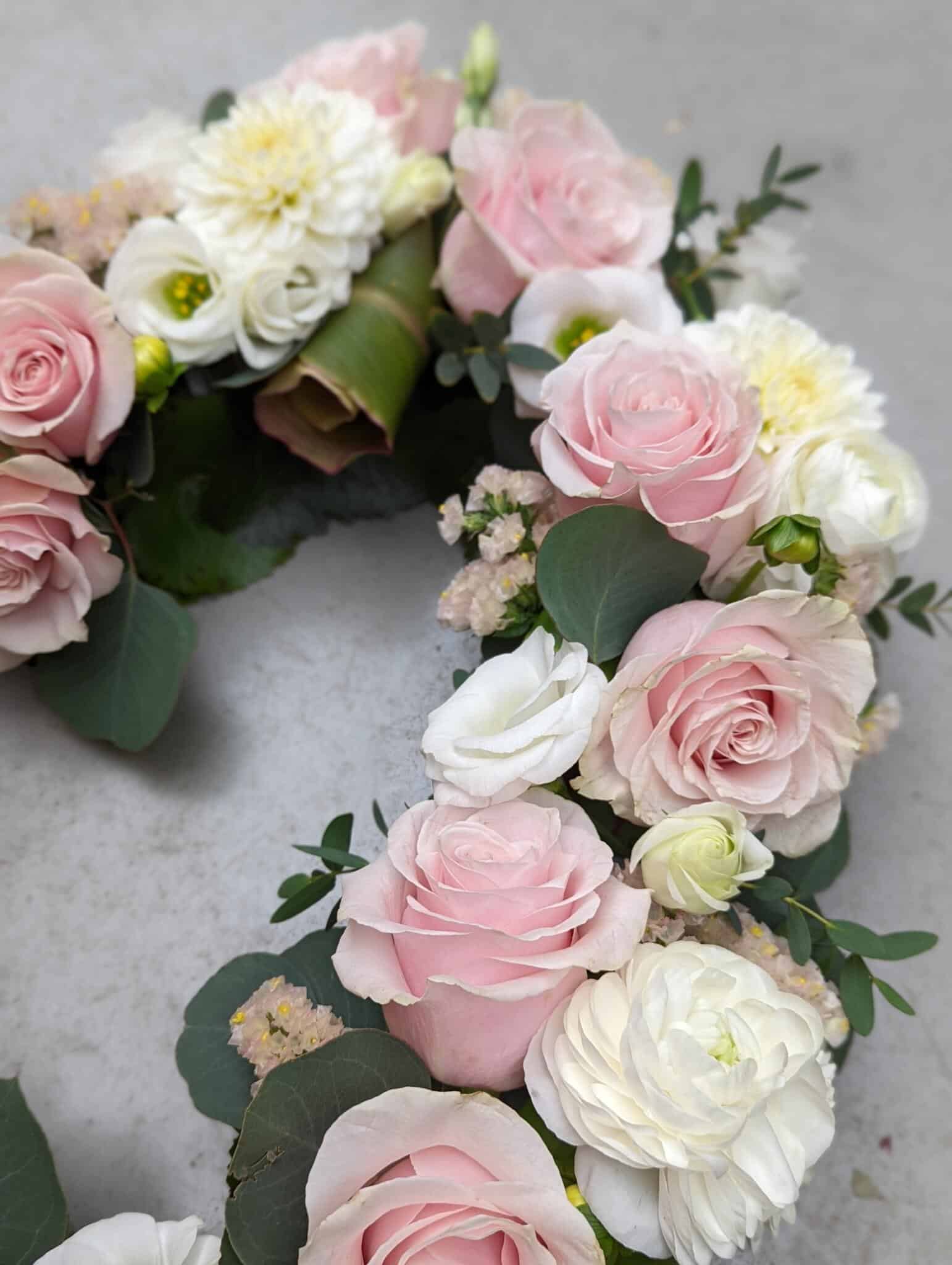 A close up of soft pink roses, white lisianthus, white rununculus, and blush statice in a open heart design.